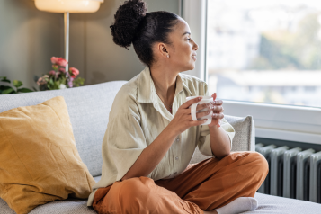 A photo of a person sat in a living room holding a warm brew.