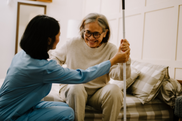 A photo of an elderly woman in her home as she helped to stand by a nurse.